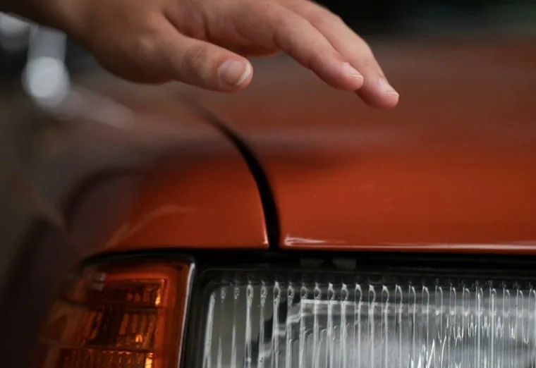 a hand inspecting a car's headlight and bodywork